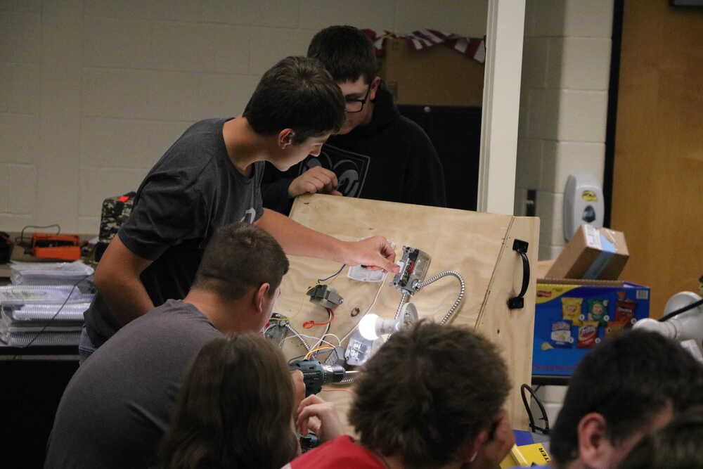 HVAC classroom at Hamilton High School, three male students help wire electrical.