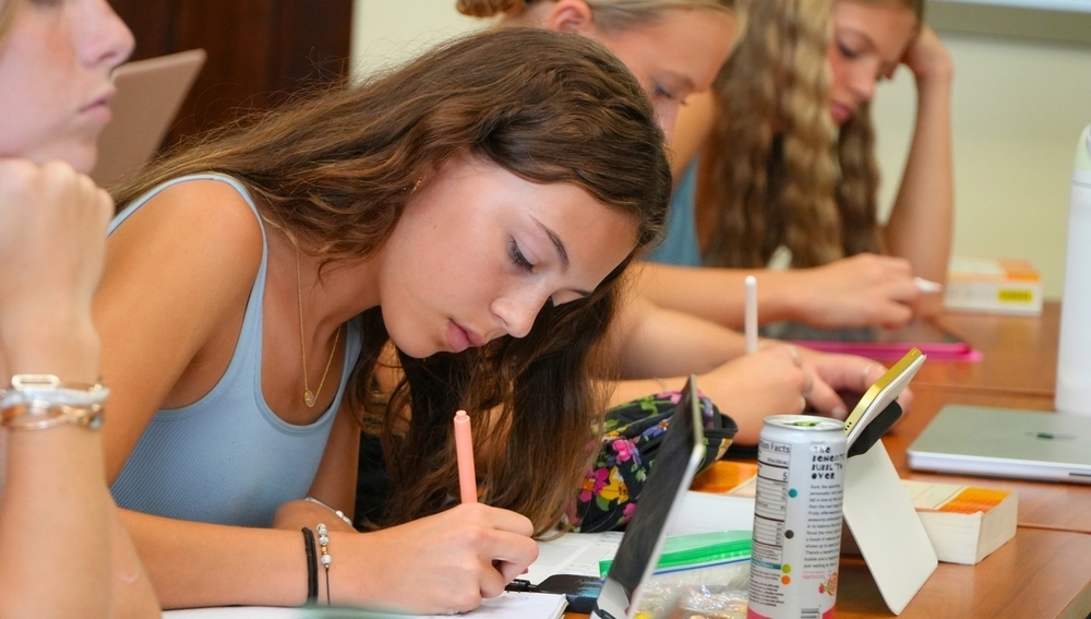 A female student writes on a piece of paper in a college setting.