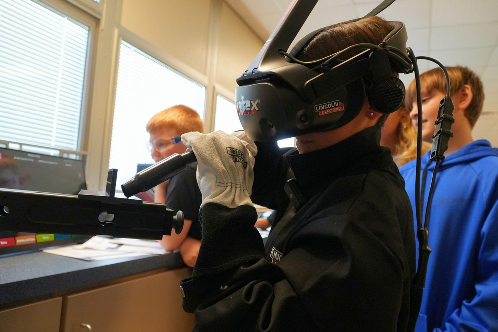 A male student with brown hair with a black virtual reality headset and welder.