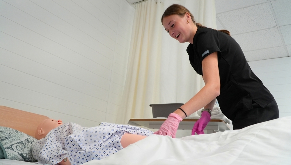A student smiles while doing medical work on a dummy.