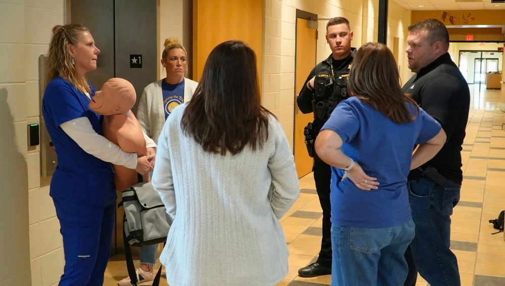 A group of adults stands in a circle with a dummy.