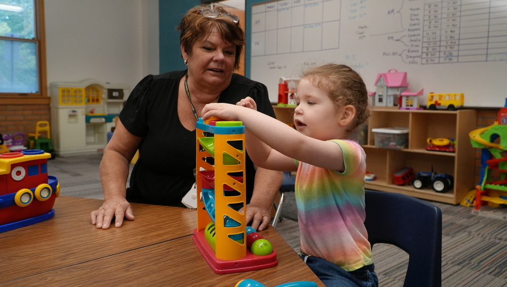 A female teacher looks on as a female student plays.