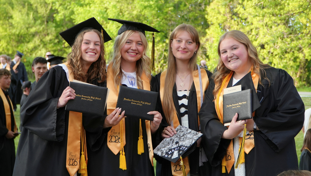 Four female Hamilton High School graduates smile with their diplomas.