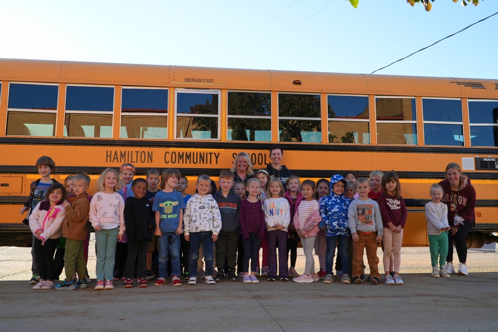 School bus safety week, two bus drivers with students in front of a big yellow Hamilton Community Schools bus.