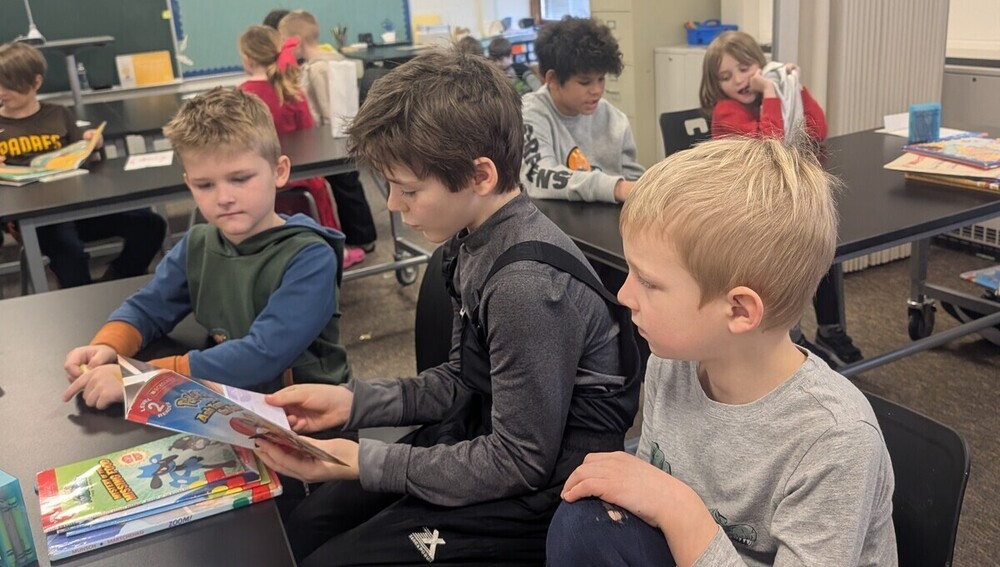 Three young students read a book together.