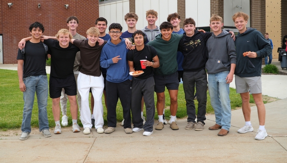 A group of male students smiles outside of a school.