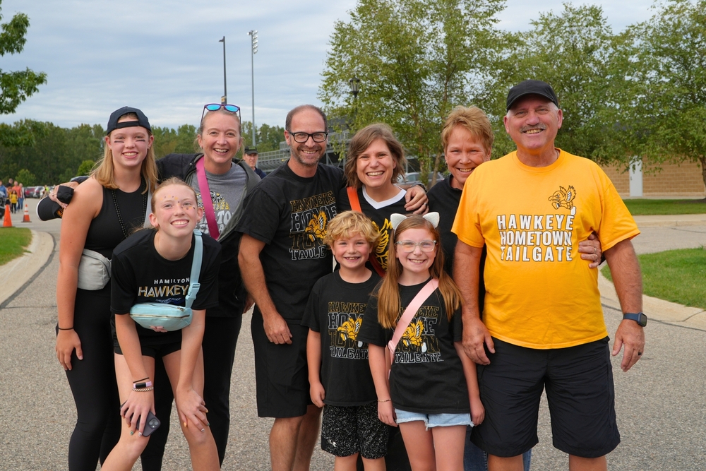 Adults and students come together and smile in front of a stadium.