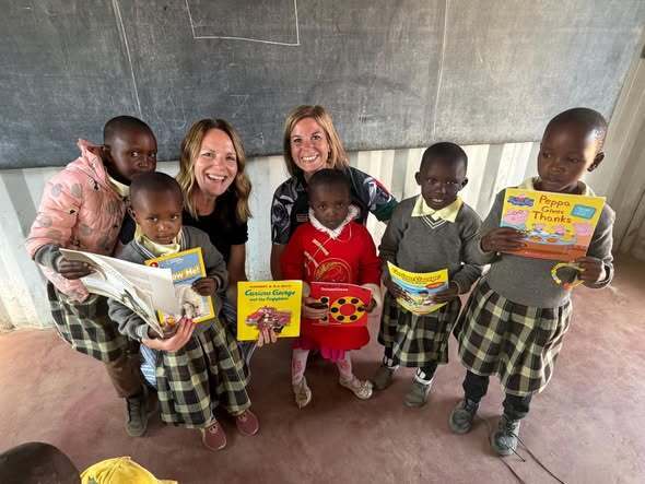 Two teachers stand in the middle of students holding up books in a classroom.