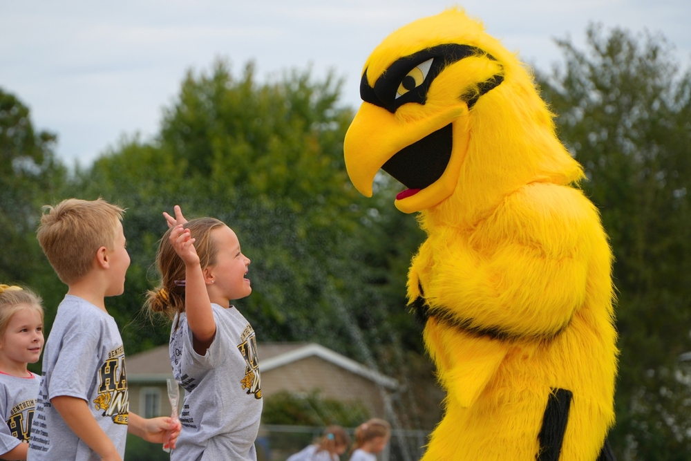 A female and male student smile looking at the yellow Hawkeye mascot bird.