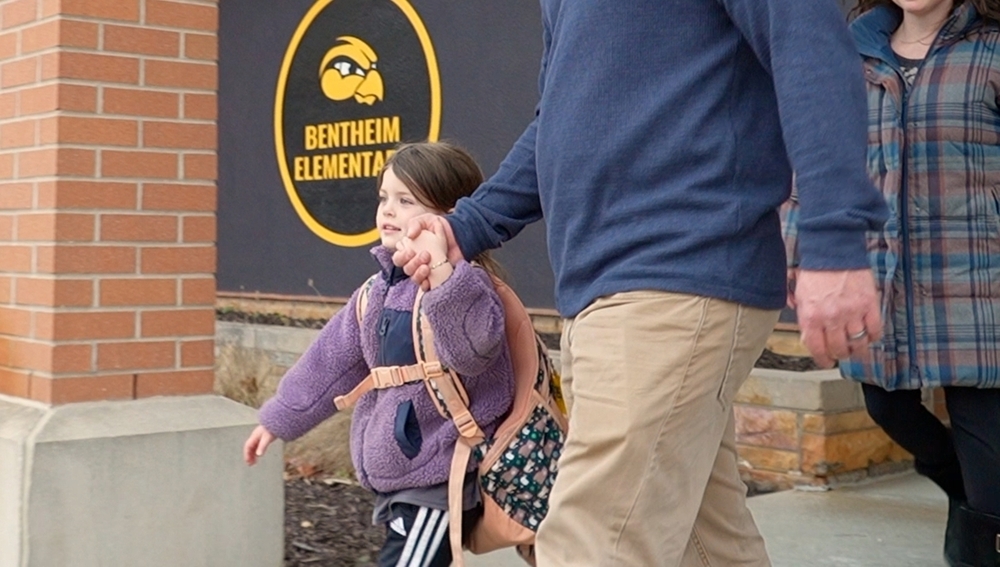 A student holds hands with her father walking out of Bentheim Elementary.