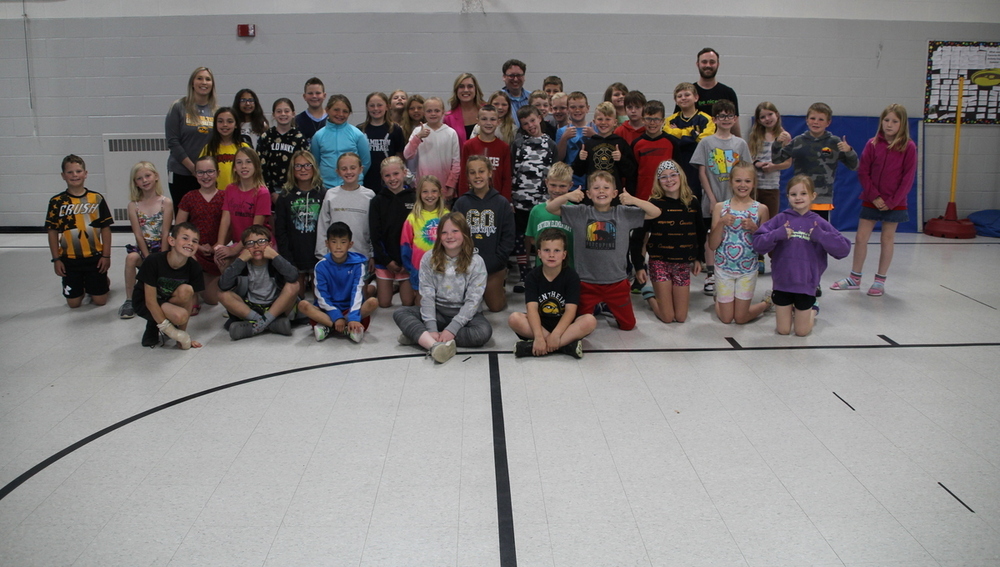 A group of students and teachers with two guests in a gym.