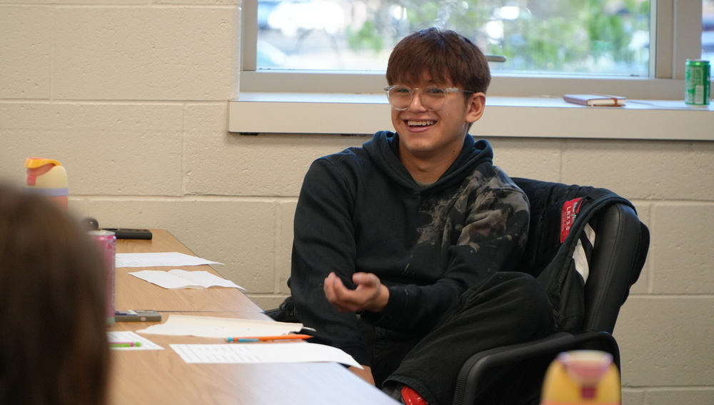 A student smiles in a college classroom setting.