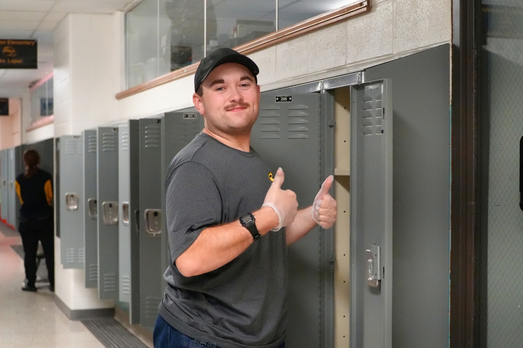 A Hamilton male staff member stands by a locker with thumbs up.