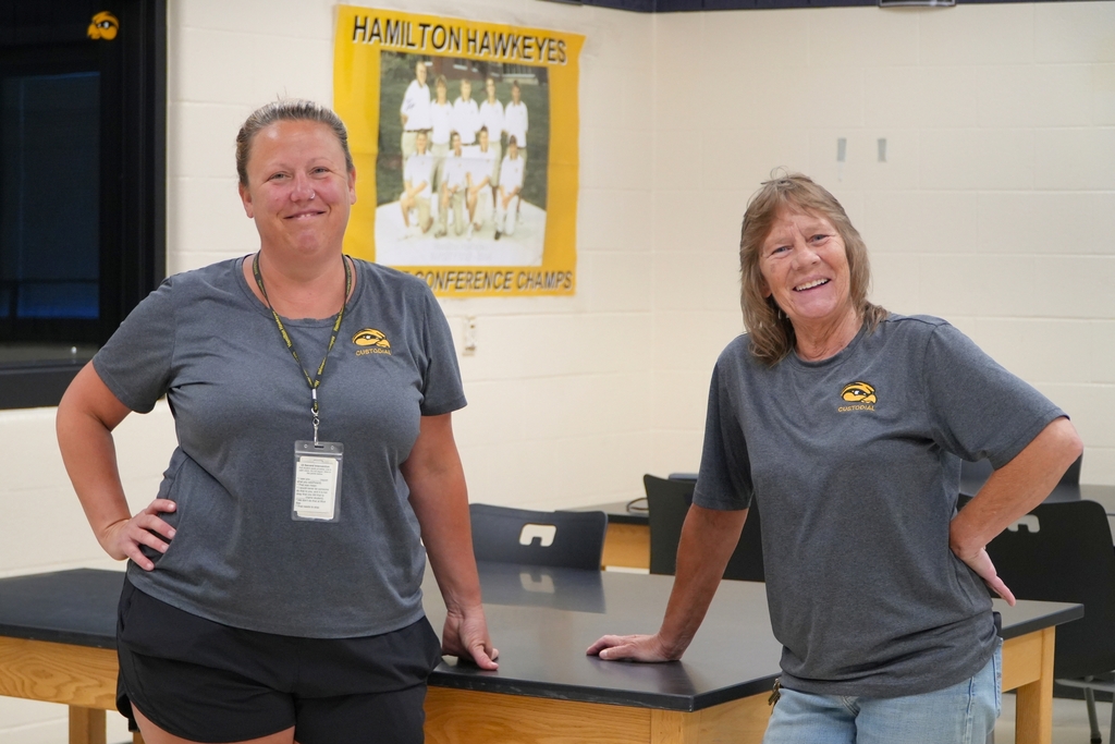 Two female staff members stand together and smile in a classroom.