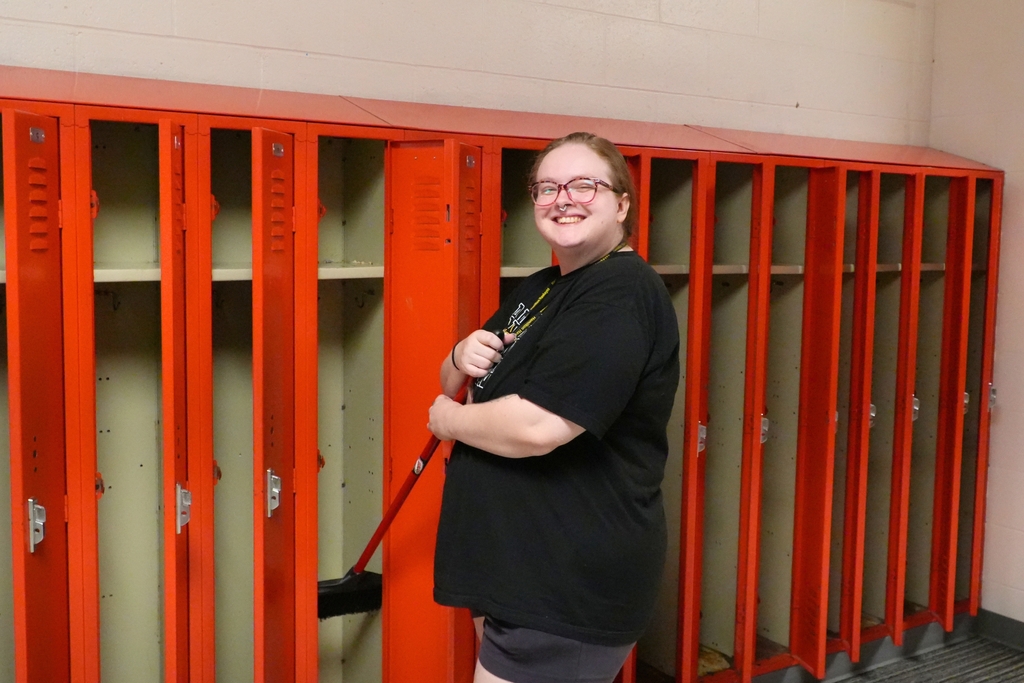 A female staff member smiles in a hallway by open lockers.
