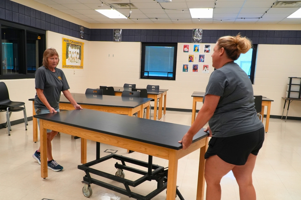 Two female staff members move a table across a classroom.