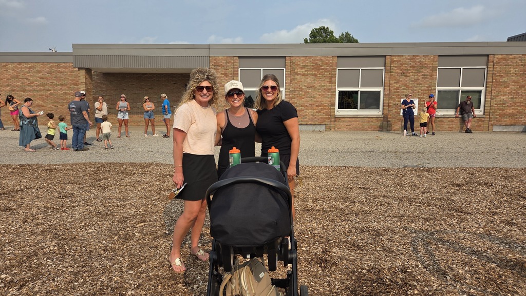 Three female adults smile in front of a brick building.