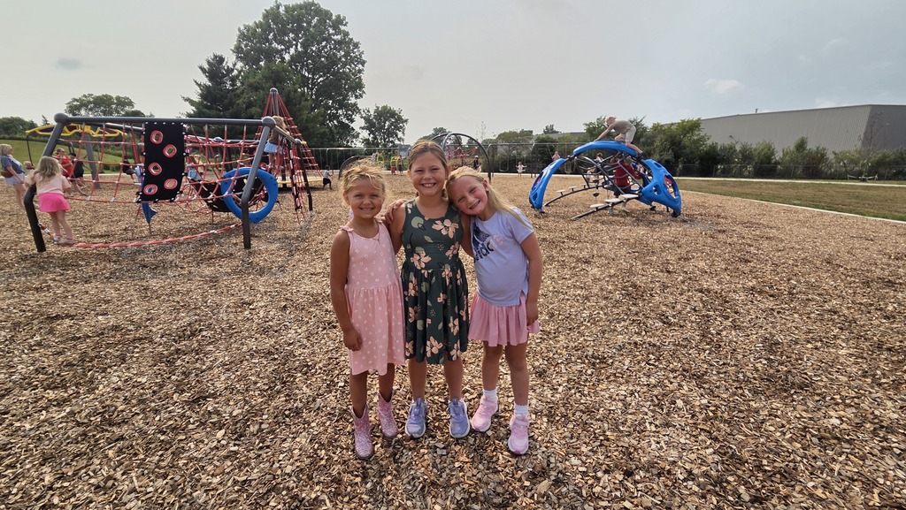 Three young female students smile together on the playground.
