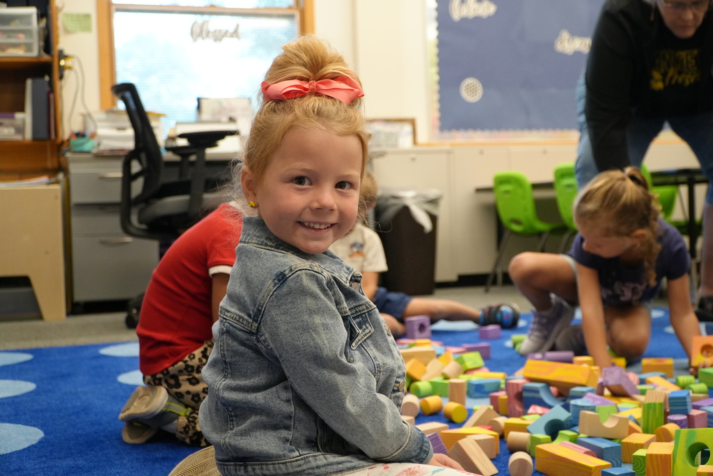 A female preschool student plays on the floor and smiles.