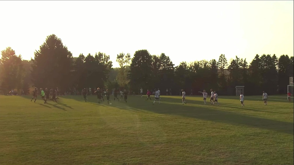 A soccer game with a sunset behind the trees.