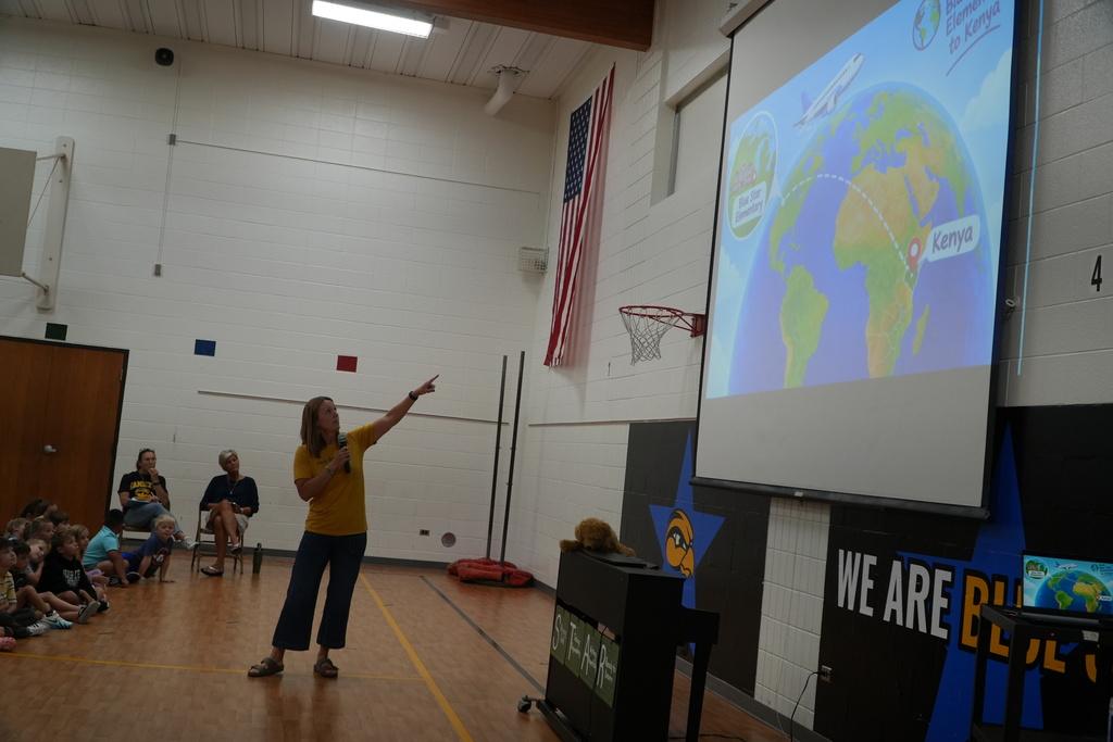 Mrs. Vruggink points to a projector screen with earth on it.