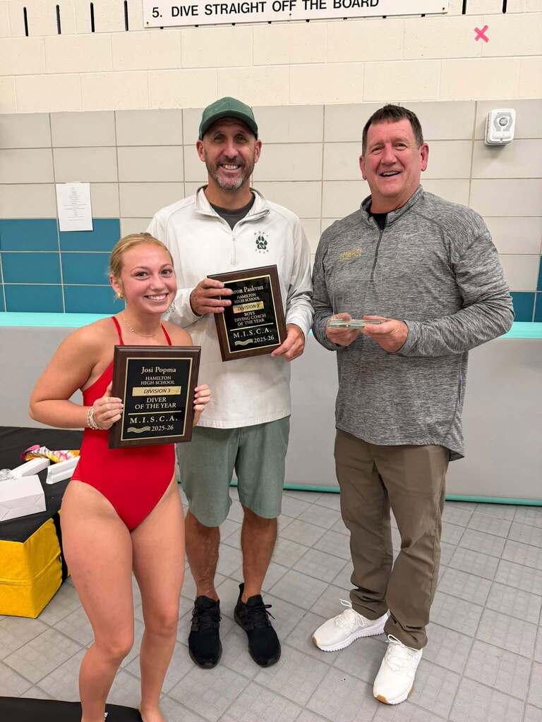 A female diver, and two male coaches smile with plaques.