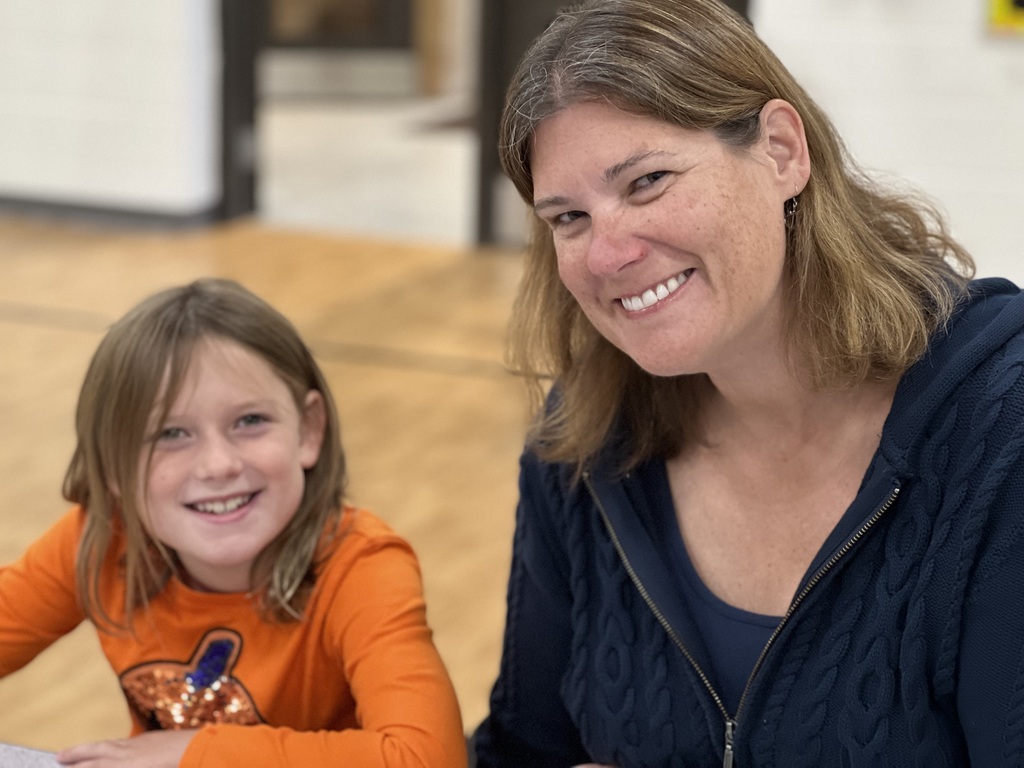 A female and student smile inside of a gymnasium.