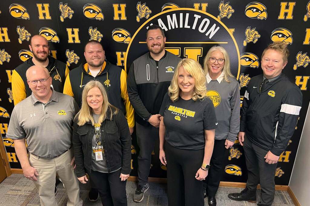 Hamilton Community Schools smiling in front of a Hamilton Hawkeye wall.