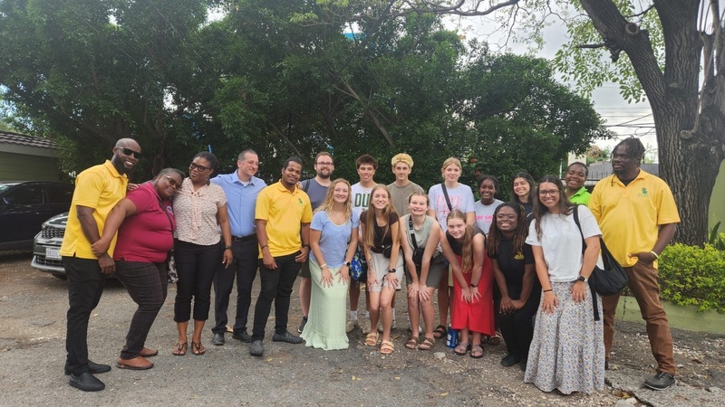 A group of adults standing in a line smiling with trees behind them.
