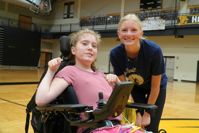 Two female students smile in a gymnasium.
