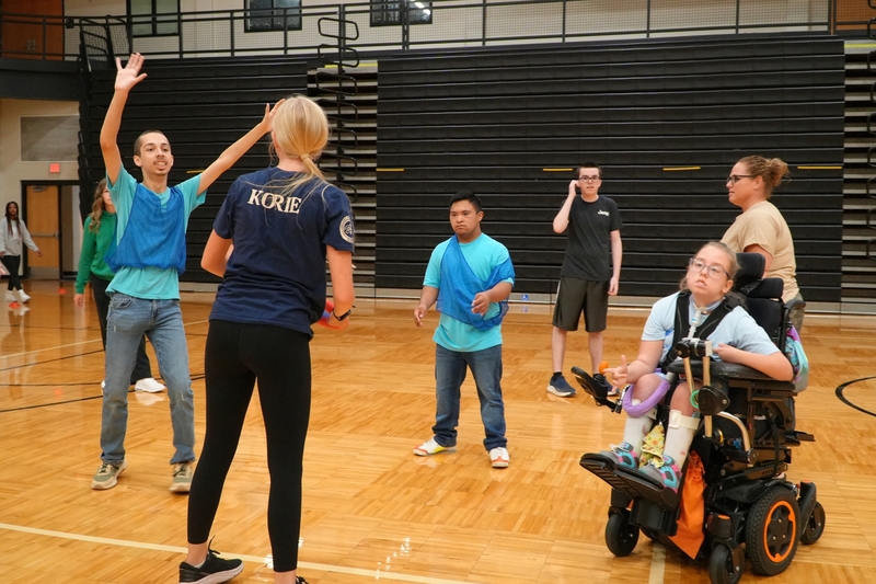 A student holds a frisbee in front of five other students in a gymnasium.