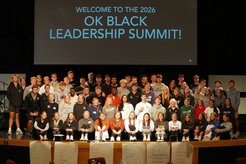 Students smile on a stage with 'Welcome to the 2026 OK Black Leadership Summit' behind them on a screen.