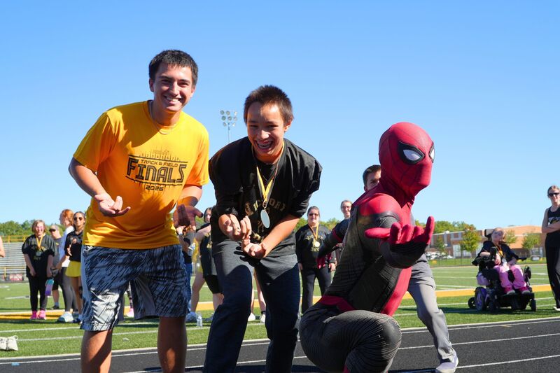 A male student, male athlete, and Spiderman pose for a photo.