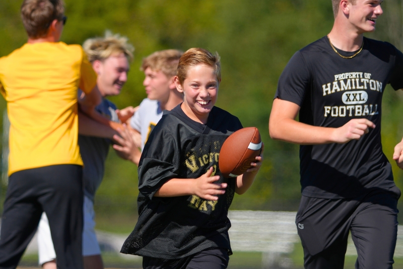 A male student runs with a football while smiling.