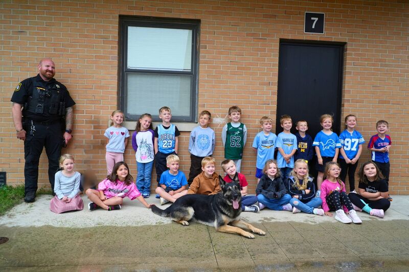 A kindergarten class with a police officer and K9 dog outdoors.