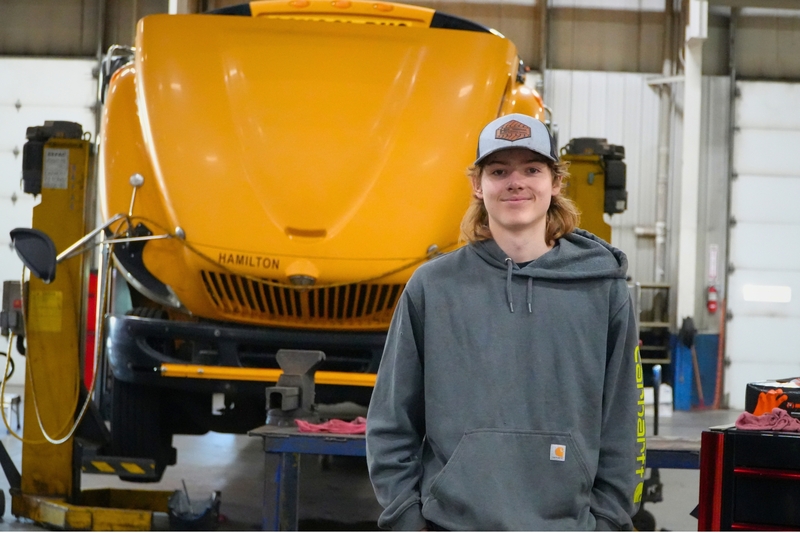 Ethan Chambers smiles in front of a Hamilton school bus with the hood up.