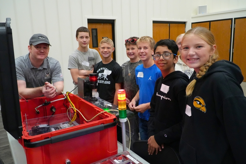 Students in a group stand and smile around an electrical circuit.
