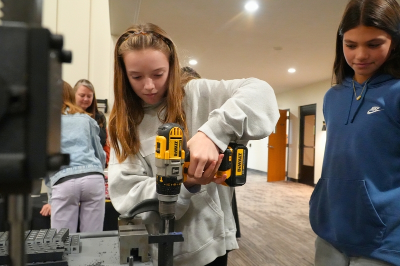 A female student uses a drill near a press.