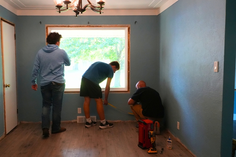 A teacher and two male students help measure a wall.