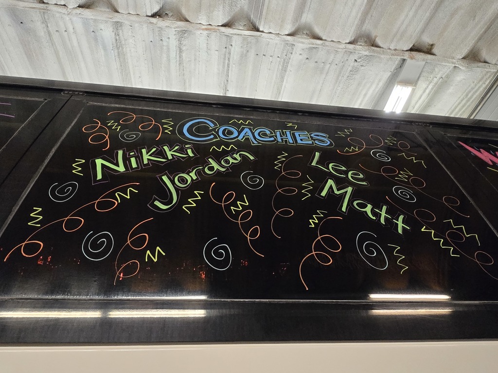 Photos of decorations on the bus windows for the high school volleyball bus that will taking the team to state. This window says "Coaches" with the coaches' names listed: Nikki, Jordan, Lee, Matt