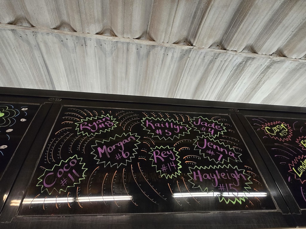 Photos of decorations on the bus windows for the high school volleyball bus that will taking the team to state. This window has some of the players names and jersey numbers: Ryan #8, Morgan #6, Coco #11, Kaitlyn #5, Rey #14, Jade #4, Jenna #7, Hayleigh #15.