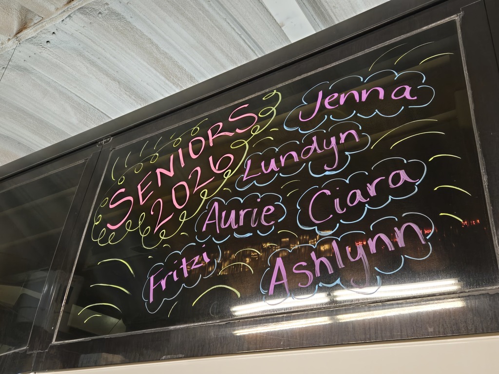 Photos of decorations on the bus windows for the high school volleyball bus that will taking the team to state. This window says "Seniors 2026" with the names of the seniors on the volleyball team: Jenna, Lundyn, Aurie, Ciara, Fritzi and Ashlynn.