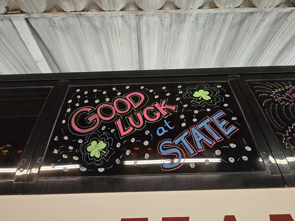 Photos of decorations on the bus windows for the high school volleyball bus that will taking the team to state. This window says "good luck at state" and has clovers around it.