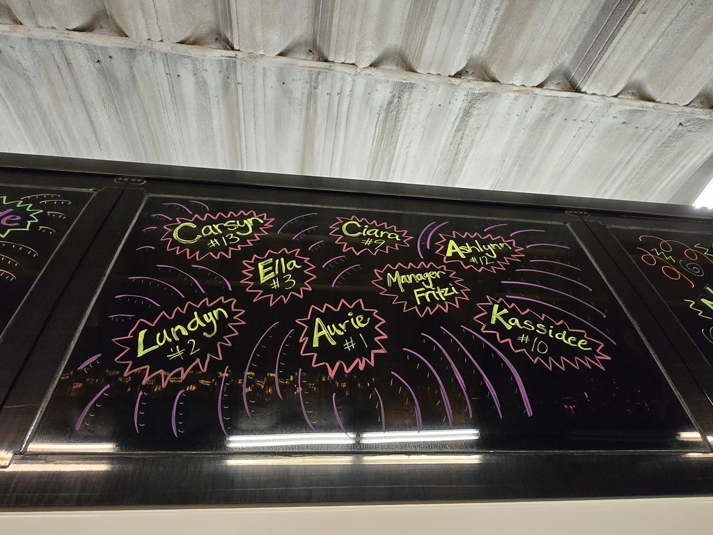 Photos of decorations on the bus windows for the high school volleyball bus that will taking the team to state. This window has the names and jersey numbers of some of the players: Carsyn #13, Ciara #9, Ashlynn #12, Ella #3, Lundyn #2, Aurie, #1, Manager Fritzi, Kassidee #10.