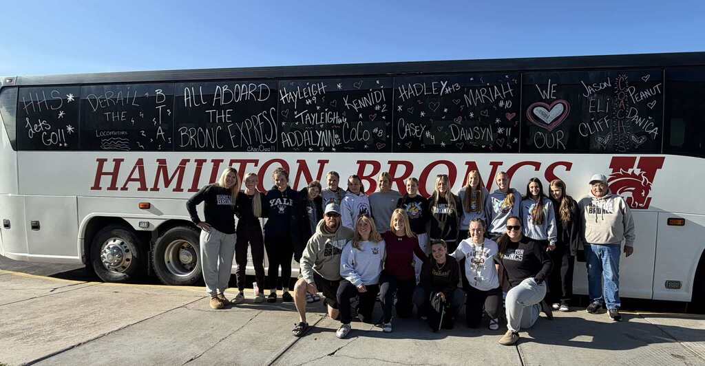 Softball team posing with the bronc bus decorated for the state final