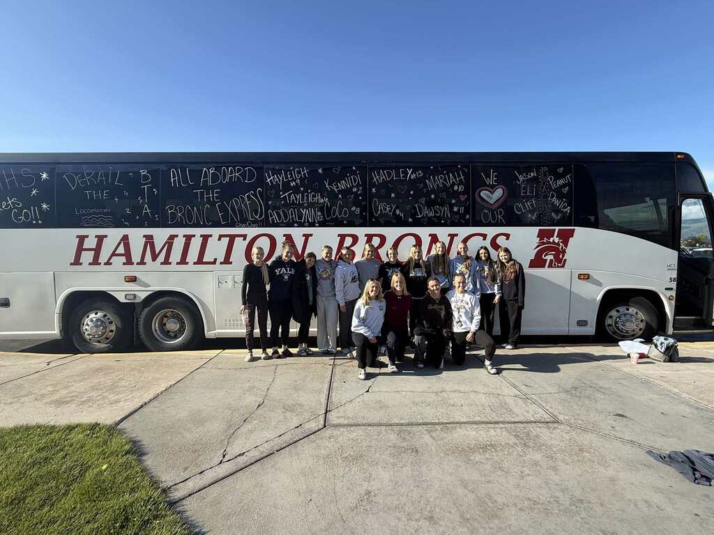 Softball team posing with the bronc bus decorated for the state final
