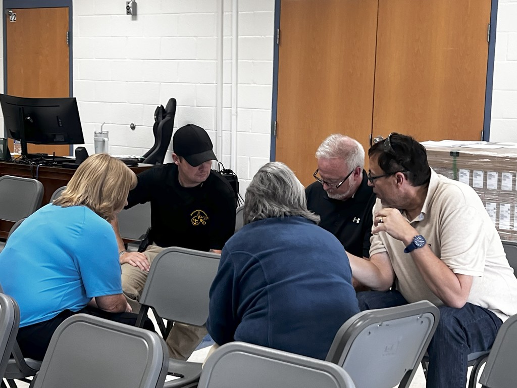 Participants gather around tables in a bright training room. Some are taking notes while others lean forward in discussion, practicing responses to a Stop & Think drill.