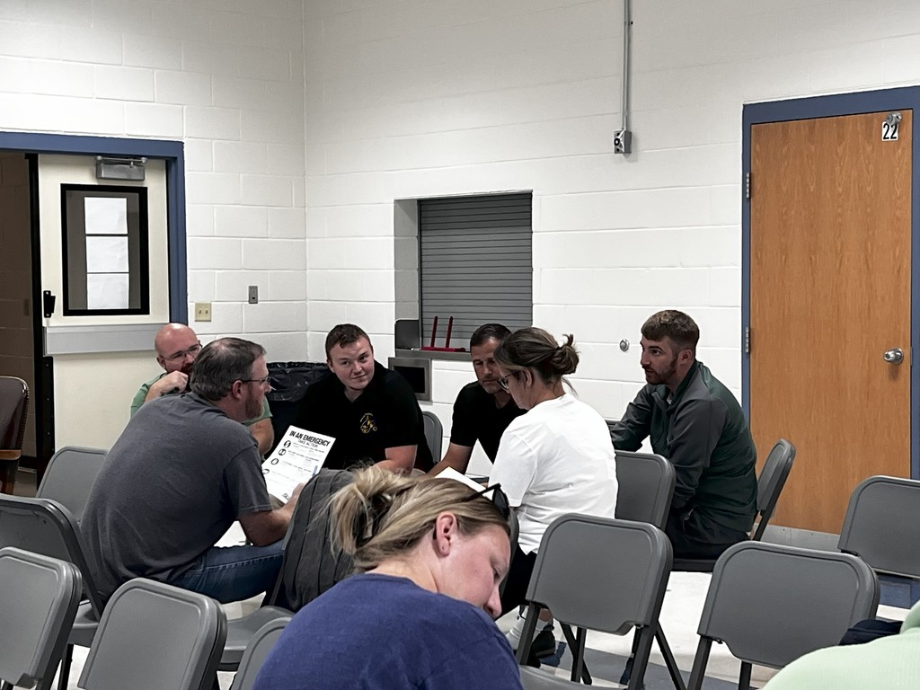 A wide view of multiple staff members seated together in a classroom, participating in group roleplay. Everyone is focused and engaged, representing collaboration from different school roles.