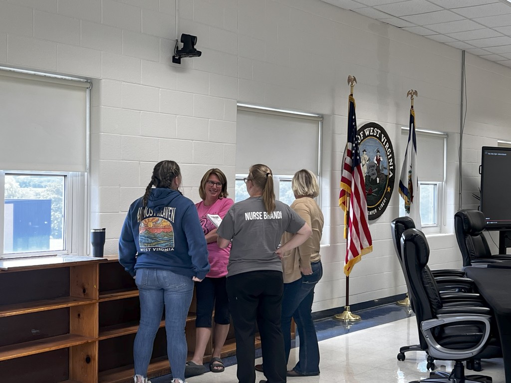 A staff group leans around a table, with one man actively explaining a point while others follow closely. The atmosphere is serious, reflecting active engagement in the safety drill.