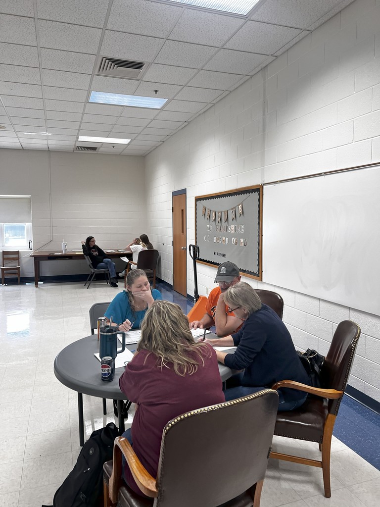 A group of staff members sit around tables in a classroom, leaning in as they listen to a speaker. Several people look attentive and engaged in discussion, showing collaboration during the safety training.